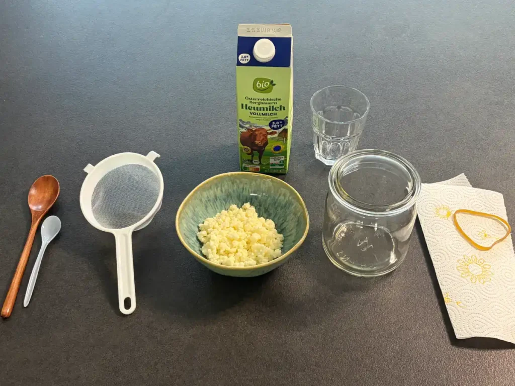 Zutaten um Kefir selber herzustellen: Kefirknollen, Milch, Kunststoffsieb, Holz oder Plastiklöffel, großes Glas, Abdeckung